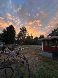 A jungle gym play structure and part of a red barn sit in front of a sunset on a farm.