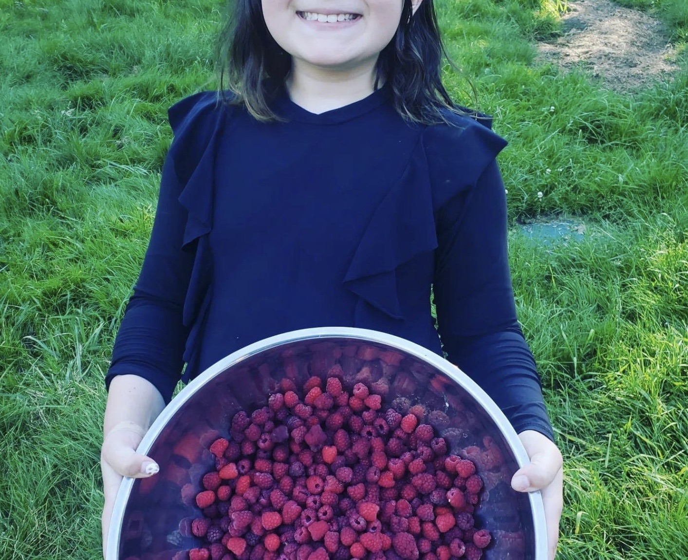 A photo of a young girl holding a large bowl of freshly picked raspberries.