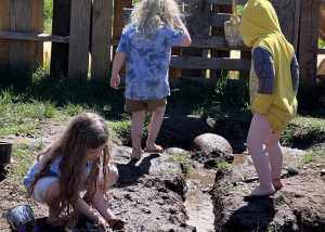 Three small children are playing in the mud near a small moat of water.